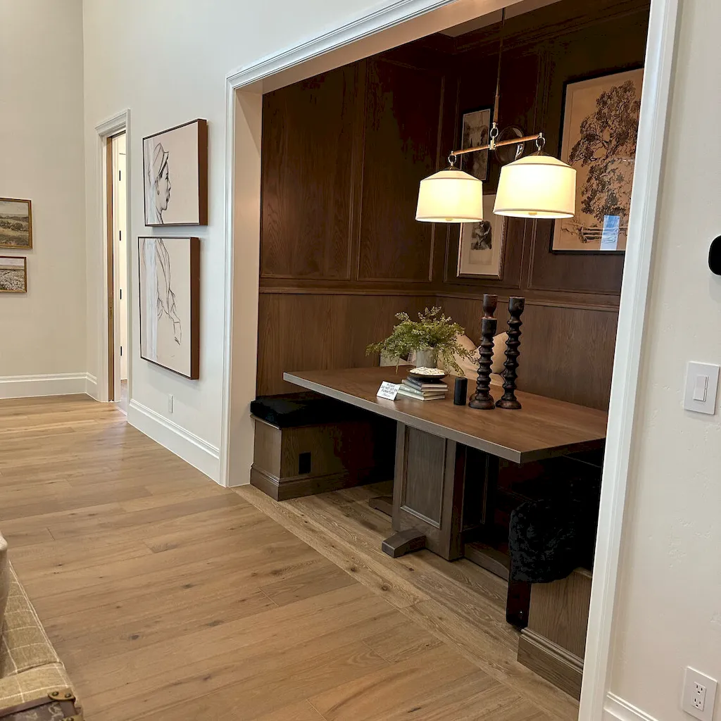 Light oak hardwood flooring in a bright hallway opening to a custom dark wood-paneled breakfast nook.